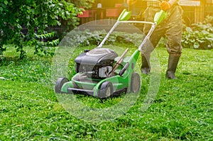 Green gasoline lawn mower on the grass in the park on the lawn