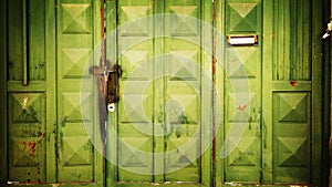 Green gate made of rusty metal sheet secured with padlocks