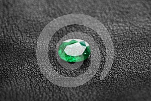 A green emerald gemstone sits on a black surface