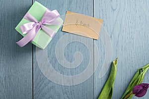 Green gift box on blue wood table with paper card for 8 march