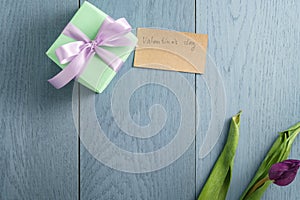 Green gift box on blue wood table with paper card for valentines day