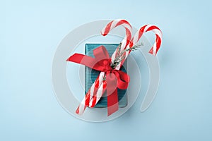 Green gift box with christmas candy cane and red bow on blue background
