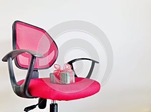 A Green gift box on red wheels office chair over off white background.