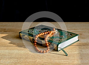 A green and gilded book of Quran and a rosary