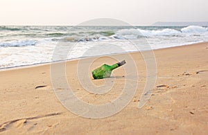 Green glass bottle with a message inside on the seashore on the