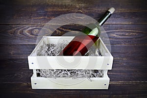 Green glass bottle of red wine with cork in wooden box with paper shavings, still life on brown wooden plank surface