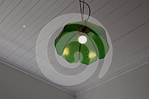 A green glass lampshade is hanging from a white ceiling, the light is on