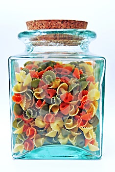 Green, glass, see through jar with cork lid containing colorful pasta shells.