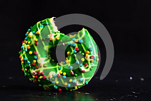 Green glazed donut with sprinkles isolated. Close up of colorful bitten donut