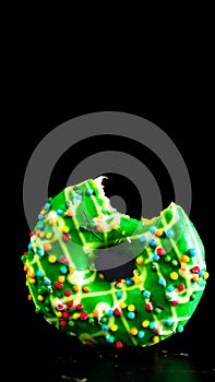 Green glazed donut with sprinkles isolated. Close up of colorful bitten donut