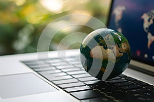 Green globe on laptop keyboard with bokeh background