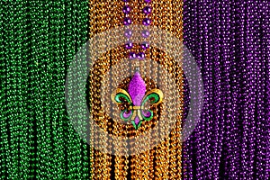 Green, gold, and purple Mardi Gras beads with Fleur de lis background