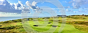 Green golf course with round bunkers with a hotel and the sea in the background photo