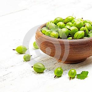 Green gooseberries in a ceramic bowl on an old wooden table