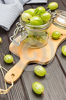 Green gooseberries in glass jar on cutting board