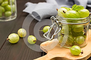 Green gooseberries in glass jar on cutting board