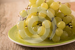 Green grapes in a plate on an old wooden background.