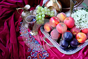Green grapes, plums, peaches, nectarines, jugs, a glass of wine, white hydrangea, a Dutch still life on a silk tablecloth, with