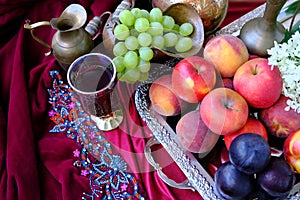 Green grapes, plums, peaches, nectarines, jugs, a glass of wine, white hydrangea, a Dutch still life on a silk tablecloth, with