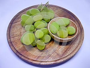 Green grapes on a round wooden plate and bowl. White background. A place to write. Juicy bunch of grapes on a wooden background