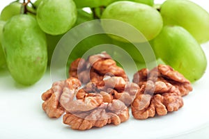 Green grapes and walnut in white plate on wooden table.