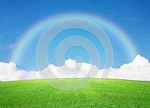 Green grass field, blue sky with clouds on horizon and rainbow