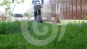 Green grass in the foreground and a man with a lawn mower moving away in the background. Low angle shot