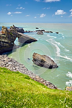 Green grass on a hillside and rocky islands in the ocean. Biarritz city and view of its the famous landmark Rocher de la Vierge, a