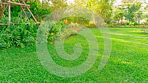 Green grass lawn in a garden with flowering plant, shurb, trees and small random pattern of grey concrete stepping stone