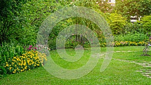 Green grass lawn in a garden with random pattern of grey concrete stepping stone , Flowering plant, shurb , trees on backyard