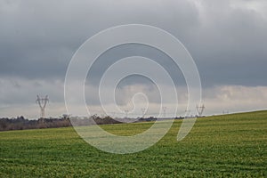 Green grass meadow, agricultural field, cloudy weather, electricity pylons in the back, natural background