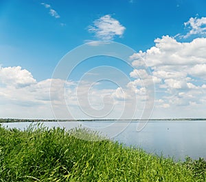 Green grass, river and clouds in blue sky