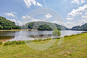 Green grassy shore of Stausee Bitburg reservoir lake with calm water, mountains with abundant trees