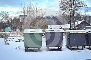 Green and grey plastic dumpster waste and garbage containers on wheels on thin snow in winter season