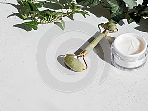 Green Gua sha massage jade roller and face cream in white container on white background