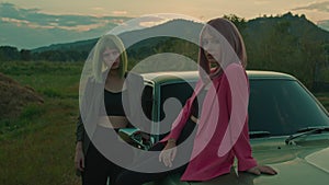 Green hair girl and her girlfriend with pink dyed hair sitting on the car outdoors