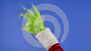 Green hairy Grinch hand showing OK gesture on isolated blue background. Gift snatcher cosplay. Christmas and new year