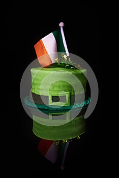 Green hat shaped green frosting cake with an Irish flag on top, to celebrate St. Patrick`s Day. reflected on metallic black