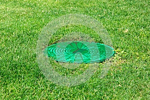 Green hatch of a sewer system in green meadow.