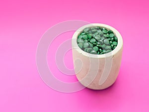 Green hawaiian spirulina in tablespoons pills on pink background. Super food, healthy lifestyle,