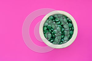 Green hawaiian spirulina in tablespoons pills on pink background. Super food, healthy lifestyle,