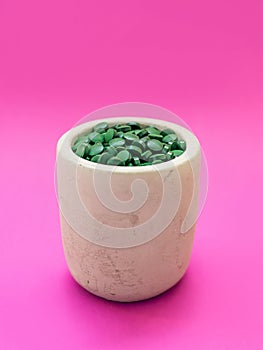 Green hawaiian spirulina in tablespoons pills on pink background. Super food, healthy lifestyle,