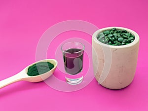 Green hawaiian spirulina in tablespoons pills on pink background. Super food, healthy lifestyle,
