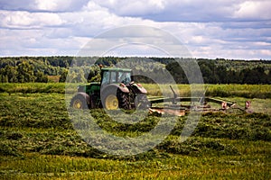 Green haymaking tractor on summer field before storm - telephoto shot with selective focus and blur