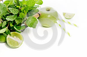 Green healthy drink ingredients on white background: lime, aapple, fresh mint and colorful paper straws. Vegetarian food. Detox