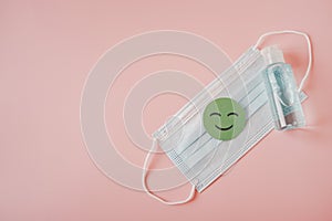 green healthy smiling face paper cut on medical face mask and bottle of blue alcohol gel on sweet pink background