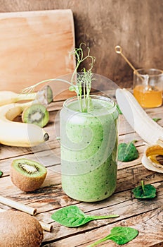 Green healthy smoothie in glass with banana, kiwi and spinach on rustic wooden background