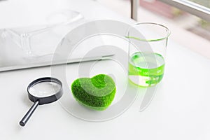 Green heart concept. Health Care researchs equipments. Green heart with a chemical organic test rube. Science glasses on laptop