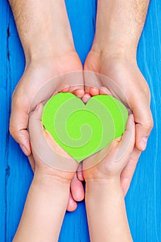 Green heart in hands of adult and child