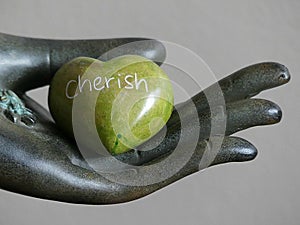 Green Heart Shaped Rock with the word CHERISH etched in it held in a decorative hand statue